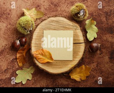 una natura morta con un biglietto bianco su una fetta di legno grezzo con castagne e foglie autunnali su sfondo marrone acquerello Foto Stock