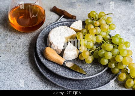 Brie e uva verde su piatto di pietra e un bicchiere di vino bianco Foto Stock