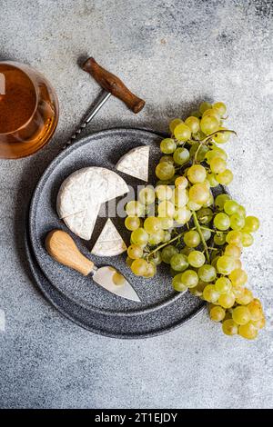 Brie e uva verde su piatto di pietra e un bicchiere di vino bianco Foto Stock
