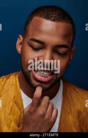 modello maschile afroamericano smiley con bretelle che guardano verso il basso con il dito sul mento, concetto di moda Foto Stock