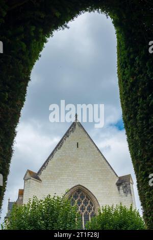 Angers, Francia, 2023. Nel giardino formale, la cappella quattrocentesca e la sua vetrata colorata sono visibili attraverso l'arco di un topiario (verticale) Foto Stock