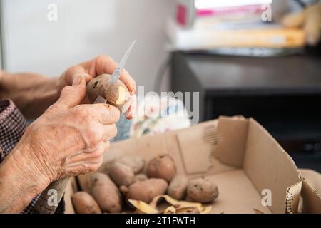 Le mani di una donna anziana che fa il lavoro domestico di pelare le patate. Mani anziane con problemi articolari, osteoartrite. Foto Stock