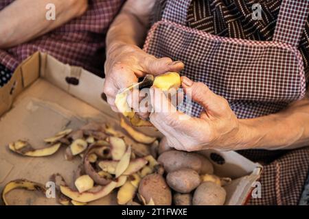 Le mani di una donna anziana che fa il lavoro domestico di pelare le patate. Mani anziane con problemi articolari, osteoartrite. Foto Stock