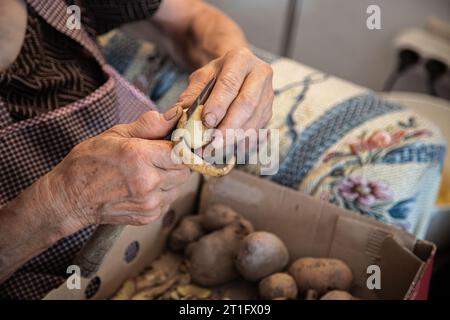 Le mani di una donna anziana che fa il lavoro domestico di pelare le patate. Mani anziane con problemi articolari, osteoartrite. Foto Stock