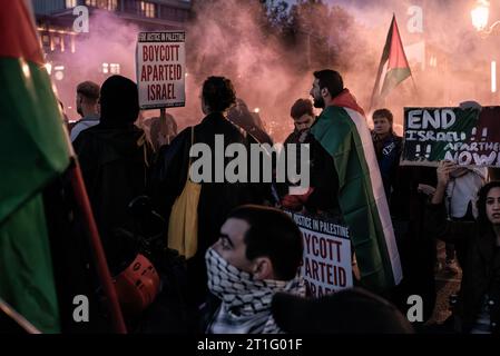 Dublino, Irlanda. 13 ottobre 2023. I manifestanti mostrano bandiere e cartelli, in mezzo al fumo di una bandierina sullo sfondo durante la dimostrazione. Il secondo giorno di proteste pro-palestinesi a Dublino. Centinaia di persone marciarono dalla guglia al ponte o'Connell in solidarietà con la Palestina. Anche gruppi come People Before Profit, Trinity BDS Movement e IPSC (movimento di solidarietà Irlanda-Palestina) hanno partecipato per mostrare la loro solidarietà. Credito: SOPA Images Limited/Alamy Live News Foto Stock