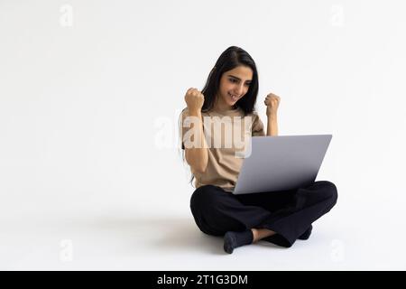 Donna aziendale indiana che utilizza un computer portatile e dà espressione vincente su sfondo bianco. Foto Stock