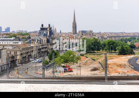 Vista della città francese di Bordeaux dall'ex quartiere portuale, con i binari ferroviari, la città vecchia e la guglia della cattedrale. Foto Stock