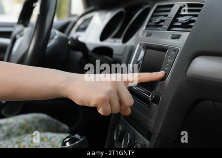 Scelta della radio preferita. Donna che preme il pulsante sull'audio del veicolo in auto, primo piano Foto Stock