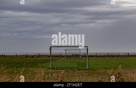 PRODUZIONE - 29 settembre 2023, Schleswig-Holstein, Hallig Langeneß: Le nuvole si muovono su un campo da calcio costruito proprio sulla riva di Hallig Oland. Foto: Axel Heimken/dpa Foto Stock