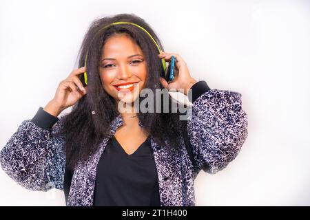 Un ritratto di una donna sorridente e attraente ispanica sulle cuffie tenere un telefono e scegliere un brano da riprodurre Foto Stock