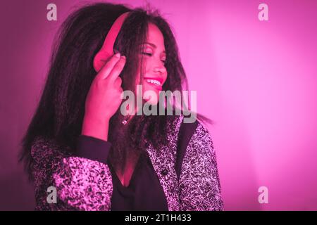 Una closeup di una giovane donna ispanica felice che ascolta la musica con cuffie di colore viola Foto Stock