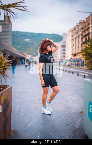 Stile di vita in città. Una giovane bruna con occhiali da sole, shorts neri, una T-shirt nera e sneakers bianche. Mettendo gli occhiali vicino a qualche piccolo Foto Stock