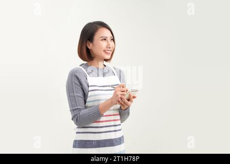 Giovane bella cameriera asiatica sorridente sicura di sé prendendo appunti su sfondo bianco Foto Stock