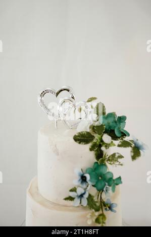 Una deliziosa torta nuziale glassata bianca decorata con un design a forma di cuore e fiori azzurri Foto Stock