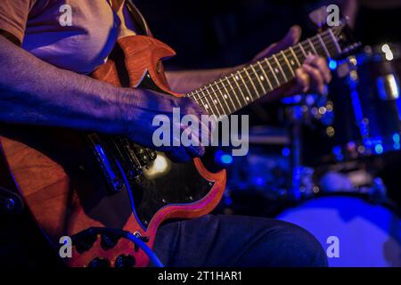 Vista ravvicinata delle mani di un uomo anziano che suona la chitarra in una jam blues in un pub di Londra con la batteria sullo sfondo Foto Stock