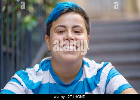 Ritratto ravvicinato di un giovane allegro con capelli blu tinti, sullo sfondo di ringhiere e scale urbane Foto Stock