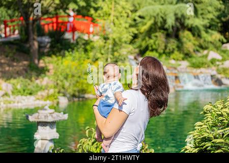 Il giardino giapponese a Digione con una famiglia, una donna con un bambino che guarda il ponte giapponese. Le jardin japonais à Digione en famille, femme avec un béb Foto Stock