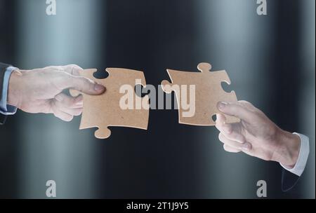 Primo piano dei partner commerciali mettendo insieme pezzi di puzzle bianchi su sfondo nero Foto Stock