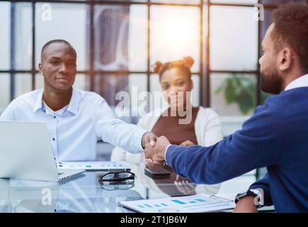 Gli uomini d'affari multietnici overjoyed scuotono le mani che salutano familiarizzandosi in ufficio Foto Stock