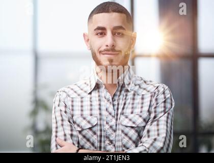 Giovane uomo d'affari bello in piedi con braccio attraversato in ufficio. Foto Stock