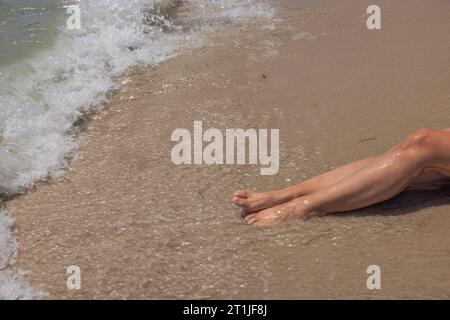 Splendida vista delle gambe delle donne sulle onde che arrivano sulla spiaggia di sabbia. Miami Beach. Foto Stock