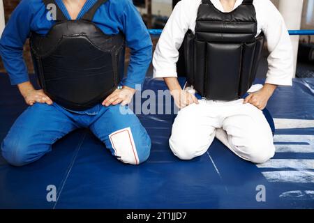 Karate, persone e inginocchiarsi, allenati con la lotta nel ring e nelle arti marziali, giubbotto di protezione con disciplina e pronto per la battaglia. Fitness, guerriero e.. Foto Stock