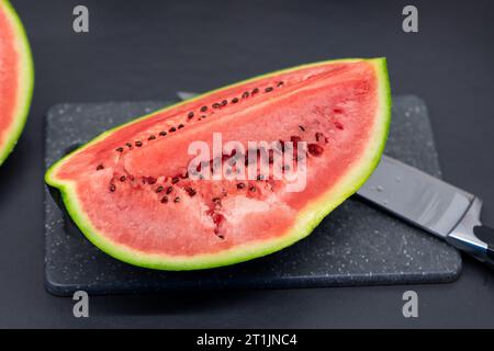 Un ritratto di un quarto di un anguria tagliata verde adagiato su un tagliere di plastica accanto a un coltello. Il pezzo o la fetta della frutta è pronta per essere mangiata Foto Stock