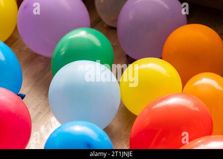Un ritratto di più palloncini vibranti che giacciono sul pavimento di un salotto al coperto di una casa. Le decorazioni divertenti sono pronte per una festa di compleanno a casa o per ann Foto Stock