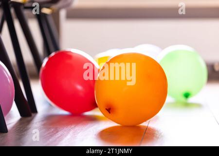 Palloncini colorati che si trovano sul pavimento di un soggiorno all'interno di una casa tra le sedie del tavolo. Le decorazioni divertenti sono pronte per una casa Foto Stock
