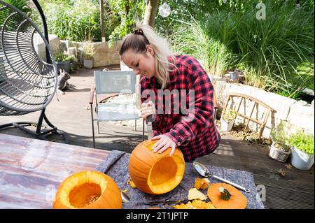 Per Halloween, una donna bionda taglia una faccia in una zucca arancione con un coltello Foto Stock