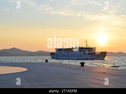 Zara, Croazia - marzo 2015: Traghetto per auto e passeggeri che passa accanto alla famosa attrazione saluti all'installazione del sole a Zara, Croazia, durante Foto Stock