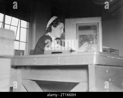 La vita al Royal Navy armamento Depot Priddy's Hard, Gosport, 25-30 luglio 1944 presso la Royal Navy armamento Depot Priddy's Hard a Gosport, 23-anno-vecchio re Vera messa azoturo di piombo agglomerati in forma di pellets nel guscio fusibili. Così delicato è questo esplosivo che ha a disposizione per lavorare con le sue mani in una scatola di localizzare eventuali esplosioni. Lei guarda attraverso una spessa triplex pannello di vetro. Foto Stock