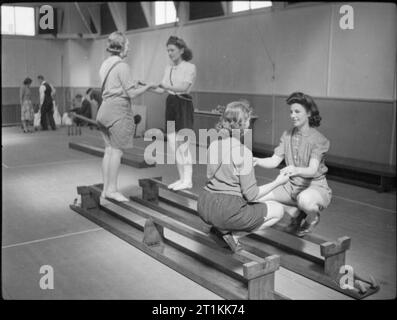 Benessere in fabbrica opera- benessere a Pilkington della fabbrica di vetro, St Helens, Lancashire, Inghilterra, Regno Unito, 1944 Donne equilibrio sui banchi capovolta in palestra presso la fabbrica un centro di riabilitazione, (probabilmente alla Pilkington di opere in vetro presso il St Helens), come parte del loro recupero dopo un infortunio. Secondo la didascalia originale 'l'obiettivo della [center] è quello di evitare che gli uomini e le donne di diventare permanentemente disabilitato. Da esercizi e massaggi sotto la guida di un fisio-terapeuta addestrato in moderni metodi i feriti sono dato trattamento ricreativo fino a raggiungere il massimo recupero dal Foto Stock