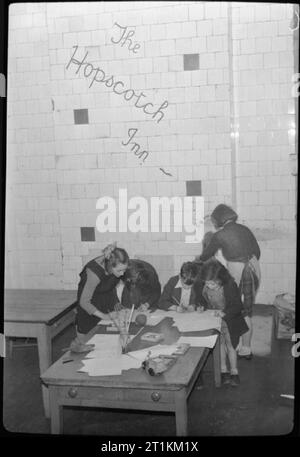 Campana Inn- il lavoro di Save the Children Fund in tempo di guerra di Londra, Inghilterra, Regno Unito, 1944 i bambini si divertono a campana Inn, un club gestito da salvare i bambini su Eversholt Street, Londra. A tavola Peggy Barker, Jean McGann, Dolly Phillips e Bobby amore disegnare, mentre un altro bambino stokes la stufa dietro di loro. Il club offre un caldo ambiente sicuro in cui i bambini possono giocare e fare amicizia. Le parole "la campana Inn' sono state dipinte sulle pareti e sono chiaramente visibili dietro i bambini. Foto Stock