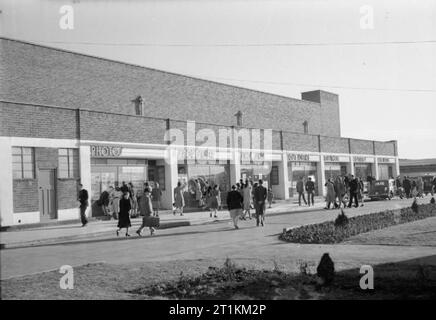 Holiday Camp ottiene andando di nuovo- La vita quotidiana in un Butlin Holiday Camp, Filey, nello Yorkshire, Inghilterra, Regno Unito, 1945 uomini, donne e bambini girovagare passato la sfilata di negozi a Butlin Holiday Camp, Filey. Da sinistra a destra, etichette sopra i negozi sono: foto, Sportswear, Lustrascarpe, Ufficio Postale, Edicola, costumi e Radio Butlin. La didascalia originale afferma che ogni Butlin's camp è un completamente autonoma città di vacanze e Filey " anche ha la sua propria stazione ferroviaria, una parte della LNER'. Il lustrascarpe è un importante negozio, perché, secondo la didascalia originale "ogni settimana un premio di una settimana" Foto Stock