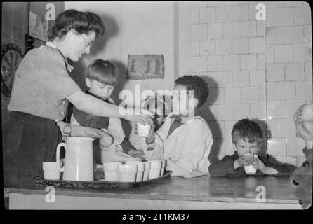 Campana Inn- il lavoro di Save the Children Fund in tempo di guerra di Londra, Inghilterra, Regno Unito, 1944 Club operaio Kathleen Fox mani una tazza di cacao e un rullo a George Megan (di 10 St Augustine's House, London, NW1) a salvare il club per bambini su Eversholt Street, Euston. George ha il padre e lo zio nell'esercito. Anche godersi il ristoro sono il Carmelo e Teresa (nascosta dal suo George) Parascandalo (di 122 Eversholt Street) e un altro giovane ragazzo sulla destra. Il Parascandalo famiglia ha vissuto su Malta per tutta la durata della guerra. Foto Stock