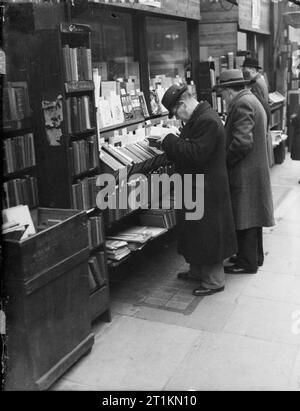 Londra in primavera del 1941- La vita quotidiana a Londra in Inghilterra due uomini leggere libri sul display al di fuori di questa libreria, da qualche parte a Londra. Gli scaffali linea il marciapiede al di fuori del negozio, consentendo ai passanti per cercare prima di acquistare. Foto Stock