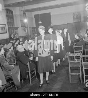 Il MEND e far fare- sartoria in classi di Londra, 1943 allievi di un London County Council sartoria classe tenere una sfilata di moda per mostrare i loro amici e familiari di ciò che hanno imparato. In primo piano è la signora Johnson, che indossa la tonaca blu è stata sposata in venti anni fa. Il vestito è stato completamente ristrutturato con la rosa e bianco seta. Dietro di lei, onorevole Hill indossa un mantello ha realizzato a partire da una coppia di portalettere pantaloni. Terzo in linea è il signor Bolton, dal Kennington classe. Foto Stock