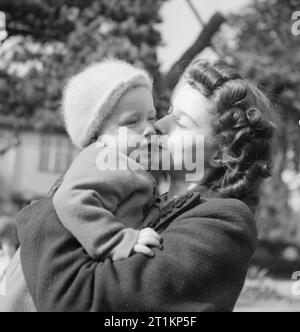 Nursery per le mamme che lavorano- il lavoro della Pietra Focaia Strada Verde vivaio, Birmingham, 1942 20 enne ra Ann Donovan detiene il suo 16 mese vecchio figlio Michael nelle sue braccia e baci lui come ella raccoglie lui dal vivaio al termine della sua giornata di lavoro. Onorevole Donovan lavora in una fabbrica di munizioni. Foto Stock