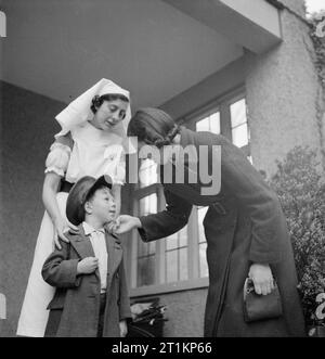 Nursery per le mamme che lavorano- il lavoro della Pietra Focaia Strada Verde vivaio, Birmingham, 1942 5 anno vecchio John Sutton orgogliosamente indossa il suo padre la vecchia PAC come egli dice addio a sua madre all'entrata di pietra focaia Strada Verde vivaio. Un infermiere si prepara alla guida John all'interno quando la sua madre, la signora Firenze Sutton, foglie per il suo lavoro in una fabbrica di mensa a 7.30. Foto Stock