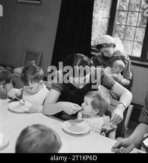 Nursery per le mamme che lavorano- il lavoro della Pietra Focaia Strada Verde vivaio, Birmingham, 1942 infermieri aiutare alcuni dei bimbi più piccoli con la loro colazione di porridge a Flint Green Road nursery, mentre altri sono in grado di nutrire se stessi. Foto Stock
