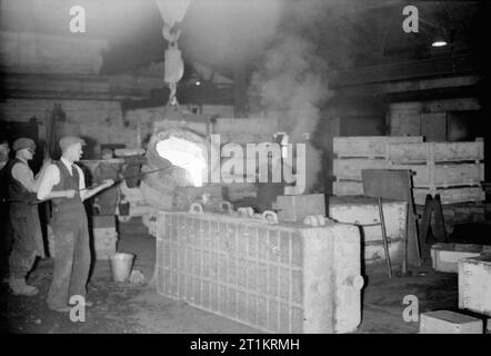 Il British Macchina Utensile industria- la fabbricazione di utensili industriali e apparecchiature, UK, 1945 lavoratori il cast del letto per un cabestano tornio in una fabbrica, da qualche parte in Gran Bretagna. Essi sono colata di metallo fuso da un grande 'siviera' in uno stampo. Alcuni degli uomini di indossare occhiali di protezione per proteggere gli occhi dalla luminosità del metallo fuso. Foto Stock