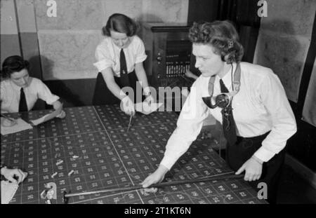 La Ragazza Ignota dietro la battaglia del mare- il lavoro delle donne del Royal Naval Service, 1942 Wren sconosciuto, indossa le cuffie e un tubo di lingua, spinge un 'ship' attraverso la griglia numerata sulla mappa della tavola di tracciatura delle operazioni stanza a HMS EAGLET. Altri due membri del WRNS possono essere visti al lavoro sul tavolo accanto a lei. Foto Stock