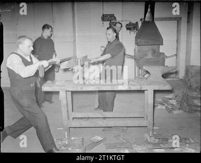 Essi hanno anche lotta che solo il supporto e attendere- gli uomini del Servizio Nazionale dei Vigili del Fuoco non guerra Extra Lavoro, London, 1942 uomini del Servizio Nazionale dei Vigili del Fuoco (NFS), lavoro metallo che hanno forgiato in cerniere per gli aerei hangar porte su un banco di lavoro realizzato localmente a Bermondsey la stazione dei vigili del fuoco. La fucina e incudine può essere chiaramente visto. Foto Stock