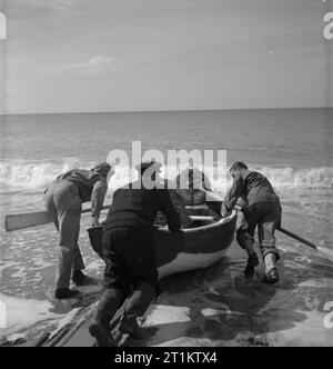 Le truppe USA in un Villaggio Inglese- La vita di tutti i giorni con gli americani in Burton Bradstock, Dorset, Regno Unito 1944 Pfc George W Burnett (a sinistra del percorso 5, Spartanburg, Carolina del Sud) e Pfc Harris L Whitwell (a sinistra della strada principale, Rogersville, Tennessee) aiutare i pescatori locali Tom Swaffield per lanciare la sua barca a remi in Dorset sunshine. Tom sta prendendo il GIs per vedere il suo astice pentole. Foto Stock