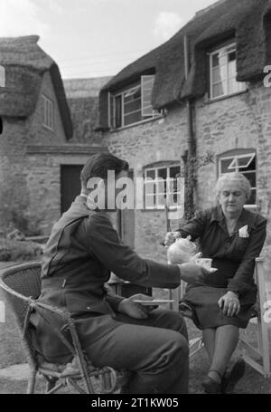 Le truppe USA in un Villaggio Inglese- La vita di tutti i giorni con gli americani in Burton Bradstock, Dorset, England, Regno Unito, 1944 La signora Howarth, moglie del villaggio precettore, versa il tè per il sergente Harold D Kregar nel giardino della sua casa in Burton Bradstock nel Dorset. Sgt Kregar è da Cheyenne Wells, Colorado e ha vinto la legione di merito in Islanda. Foto Stock