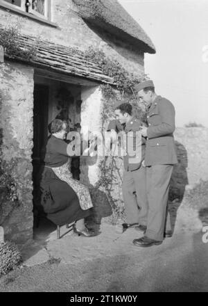 Le truppe USA in un Villaggio Inglese- La vita di tutti i giorni con gli americani in Burton Bradstock, Dorset, Regno Unito 1944 soldati americani stop per chattare con la onorevole Guyatt al di fuori del suo cottage sulla strada per il loro accampamento a Burton Bradstock, Dorset. T/4 Johnny Mandaro (di 3740 77th Street Jackson Heights, Long Island, New York) e T/5 Samuele Goodman (di 534 Ritner Street, Philadelphia, Pennsylvania) guarda come la onorevole Guyatt trecce reti al sole. Foto Stock