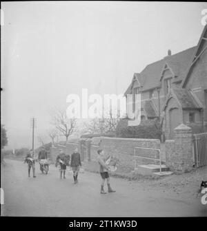 Giardini del villaggio di scolari di alimentazione- la produzione alimentare a Knighton-su-teme, Worcestershire, England, Regno Unito, 1943 Un gruppo di ragazzi che arrivano a scuola che trasportano le verdure per la giornata di pasto di mezzogiorno. Dietro di loro sulla corsia quando si avvicinano l'edificio della scuola è un uomo con una carriola piena di verdure. Tutte le verdure sono state acquistate da membri del villaggio producono l'Associazione. Foto Stock