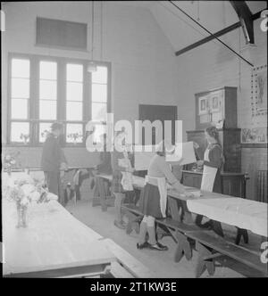 Giardini del villaggio di scolari di alimentazione- la produzione alimentare a Knighton-su-teme, Worcestershire, England, Regno Unito, 1943 Dopo il pranzo presso la scuola del villaggio di Knighton-su-teme, la sala da pranzo è cancellata e restituito al suo stato normale come un'aula. Ragazzi spostare i banchi e i tavoli mentre le ragazze ripiegare le tovaglie. Foto Stock