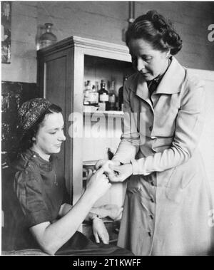 Le donne di fabbrica il lavoro di guerra a Slough Training Center, England, Regno Unito, 1941 Betty Pride riceve alcuni primi aiuti per un mal di dito dal suo supervisore femmina a Slough Centro di formazione medica della camera. Foto Stock